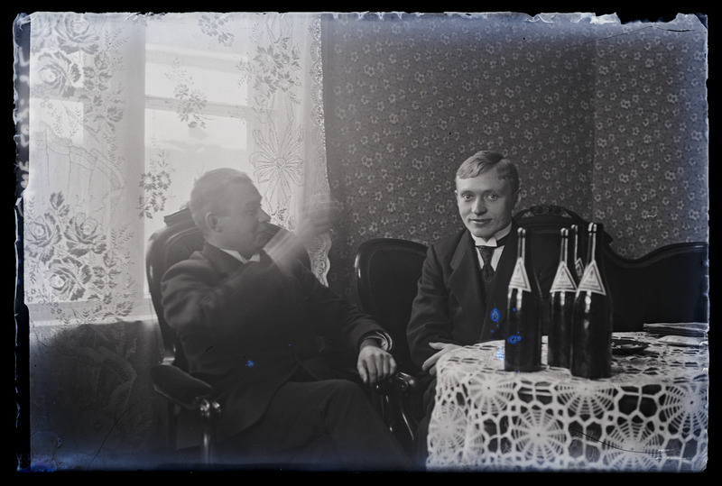 Kaks meest laua ümber istumas, pudelitega laual