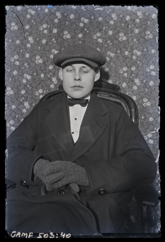 Noormehe portree, mütsi ja kinnastega. Toolil istumas