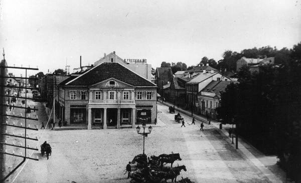 Hotell "London"  ja voorimeeste plats selle ees, Aleksandri t ( vasakul) ja Promenaadi t (paremal). 
Majade kohal kõrgub reklaamsilt: B. Frederking.  
Tartu, 1920. aastad.