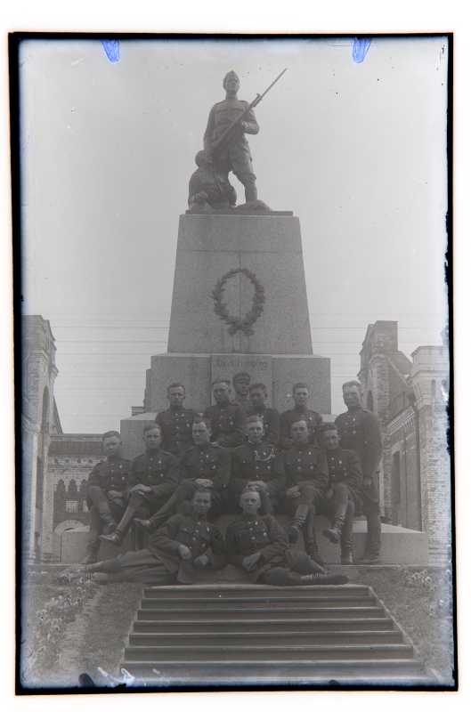 Group picture: a group of men from Tondi War School on December 1, 1924 against the backdrop of the memorial pillar of the cadets who died in the resurrection.