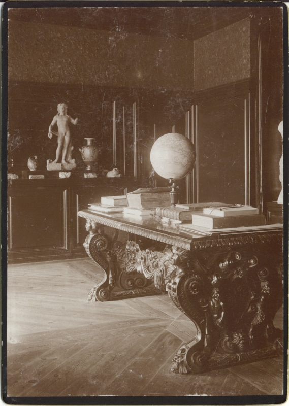 Alatskivi. Interior of the manor. In the middle of a hard baroque-style table, books and gloobus on the table; a low dark cabinet on the back side, on which sculpture, vases and so on.