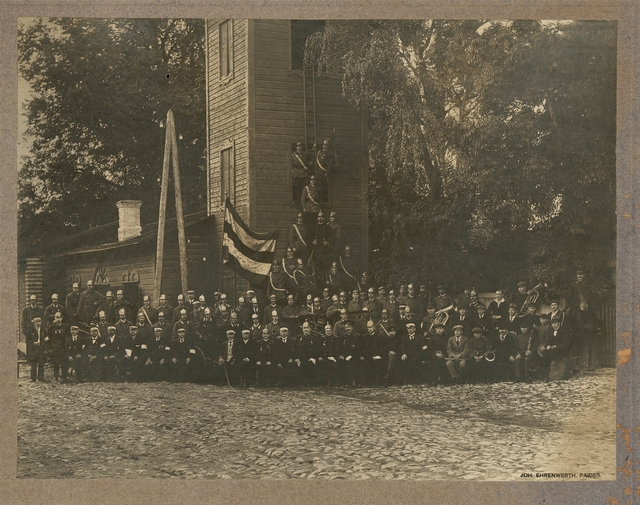 Group photo of Paide members and orchestra in the background of the spray house.