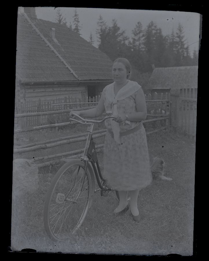 Woman with bicycle, pictured in the farmhouse, background gardens and buildings.