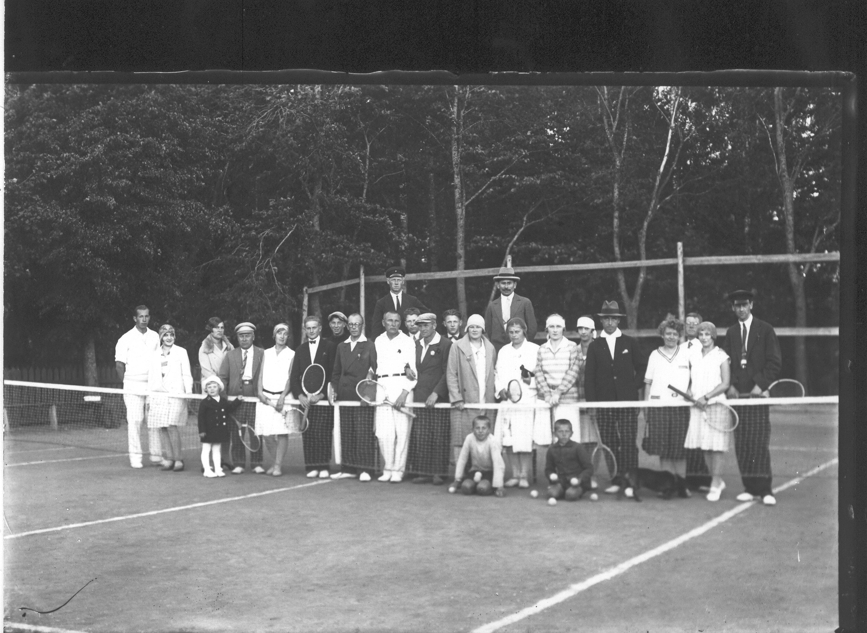 Foto. Grupp tennisemängijaid ja pealtvaatajaid Võru pargi tenniseväljaku juures.