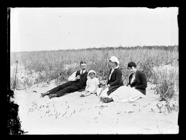 Kaks naist, mees ja laps istumas liivaluidetel