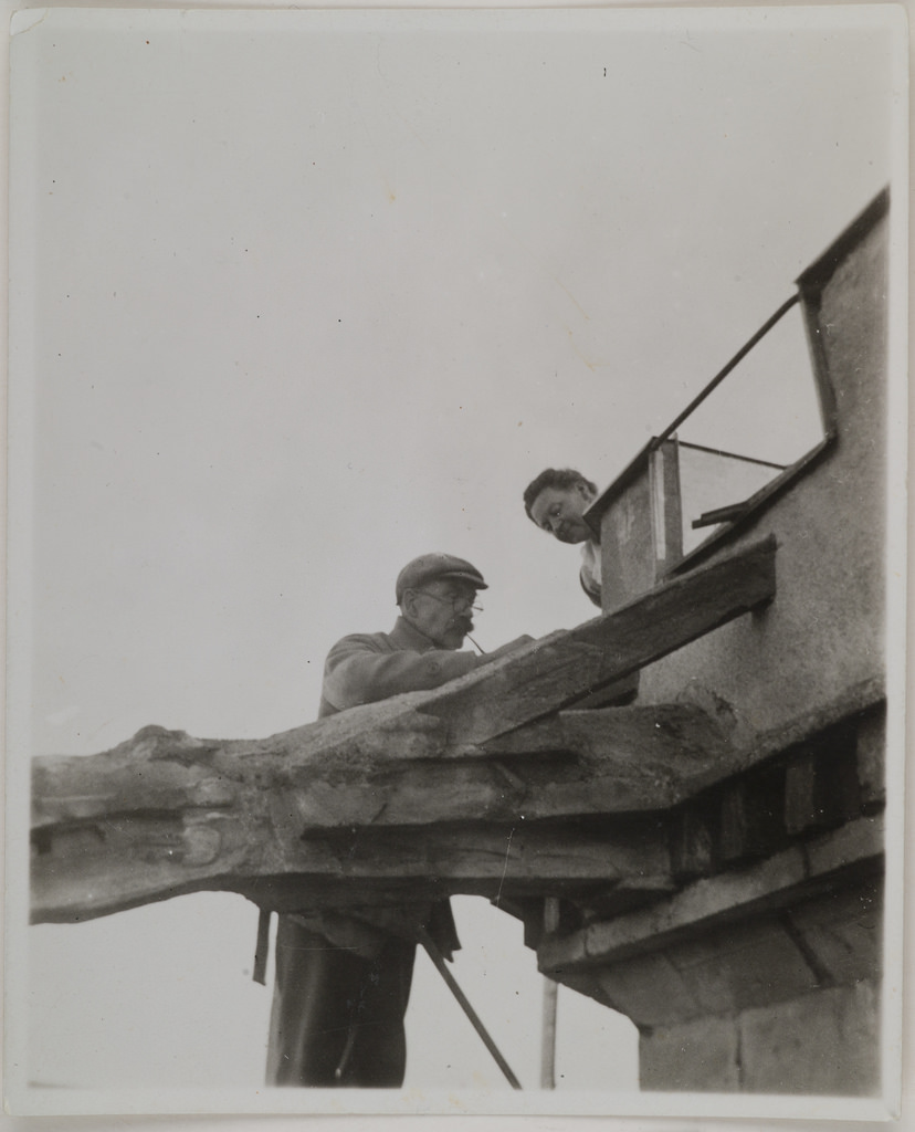 Akseli Gallen-Kallela on the tower of Tarvaspää working on a dragon-shaped gargoyle with his wife Mary watching, 1927.