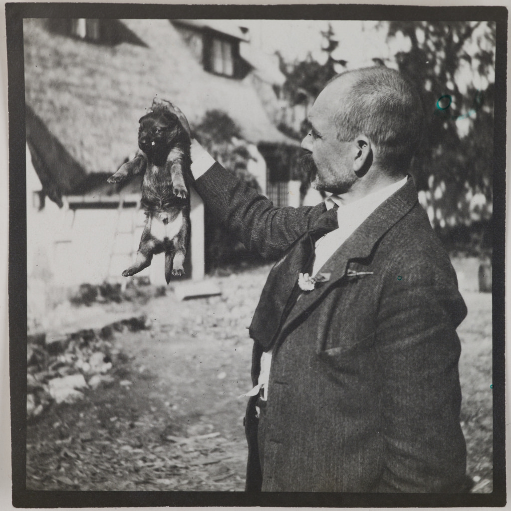 Akseli Gallen-Kallela holding a puppy in his hand at Tarvaspää, 1914.