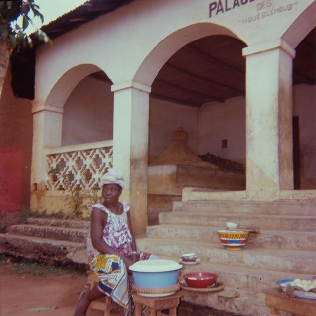 A woman sells food in front of a house with a cemetery of Zangbeto God; a personal photo