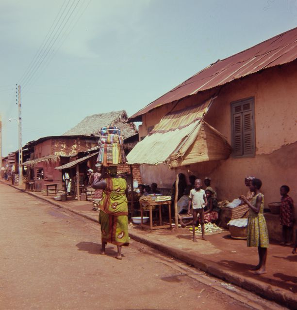A woman selling fabrics walks on the street in Porto Novo; overview