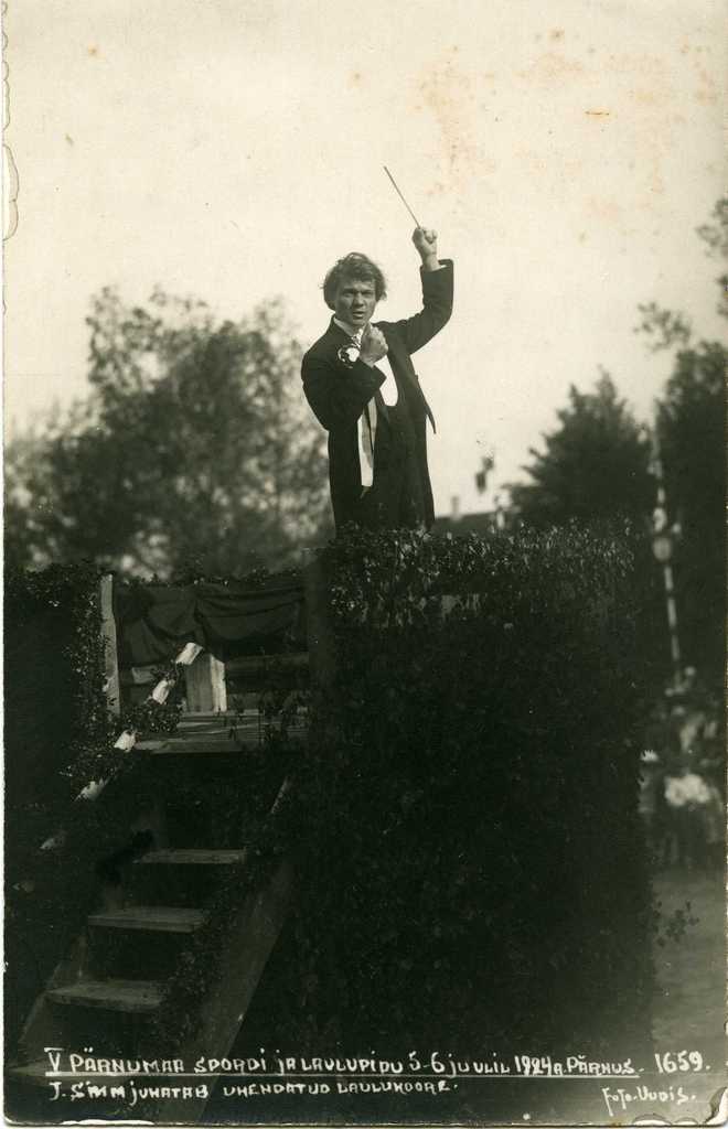 Fotopostkaart. V Pärnumaa spordi- ja laulupidu, dirigendipuldis on Juhan Simm (dirigeerides ühendatud laulukoore). 
Pärnu, 5.-6. juuni 1924.