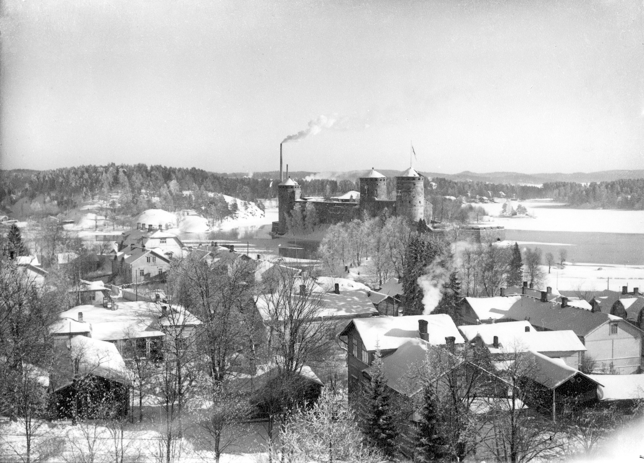 Näkymä Nälkälinnan tornista itäkaakkoon. Etualalla paljon puutaloja Linnankadun, Eerikinkadun ja Akselinkadun varrella. Keskellä Olavinlinna. Taustalla vasemmalla Kyrönniemi. talvi 1949–1950-luku. View east-southeast from Nälkälinna