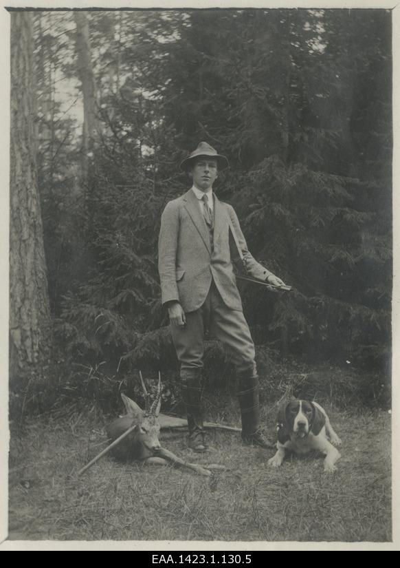 Probably Roman von Ungern-Sternberg poses under the forest with a hunting dog and a wild goat harvested for hunting