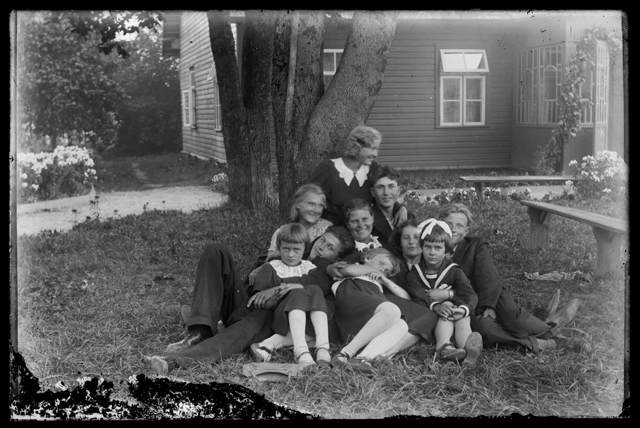 Meeste, naiste ja laste rõivastus - perekond aias, tagaplaanil elamu