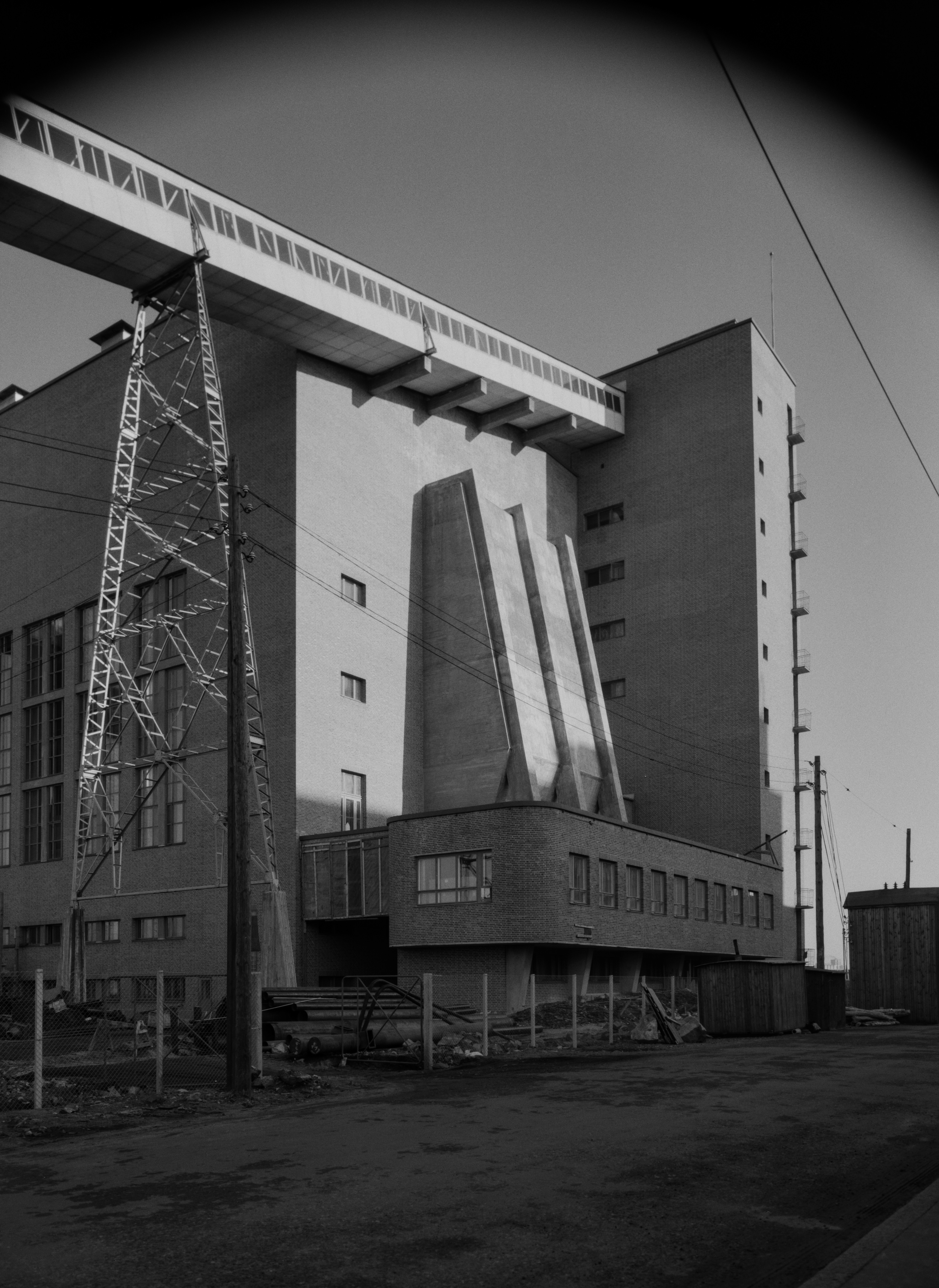 Helsingin sähkölaitoksen Salmisaaren voimala, Lauttasaarenkatu 11 (nyk. Porkkalankatu 9-11), nähtynä Tallberginkaun toiselta puolen, Porkkalankadun pohjoispuolelta. Rakennuksen yläkertaan nousee hiiltä voimalan polttoaineeksi kuljettava linjasto. Voimala A:n suunnitteli arkkitehti Vera Rosendal kaupunginarkkitehti Hilding Ekelundin johdolla, ja se otettiin käyttöön vuonna 1953. Valokuvan yläyläosassa näkyy kaareutuva tumma varjo, joka johtuu siitä, että valokuvaaja on käyttänyt kuvatessaan vastavalosuojaa.