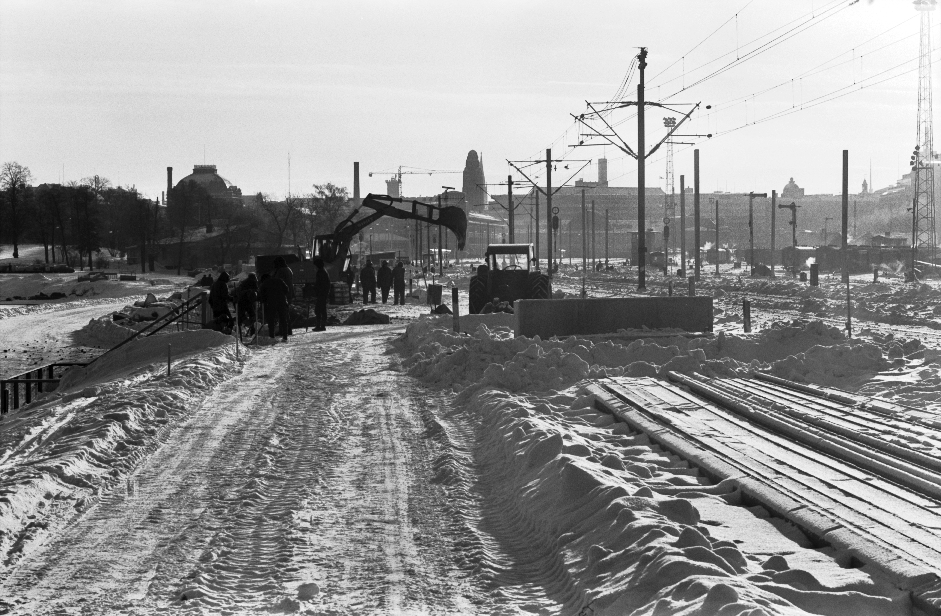 Miehiä töissä talvella lumisen pääradan varrella Eläintarhanlahden kohdalla. Näkymä Linnunlaulun suunnalta etelään. Taustalla Helsingin rautatieasema.