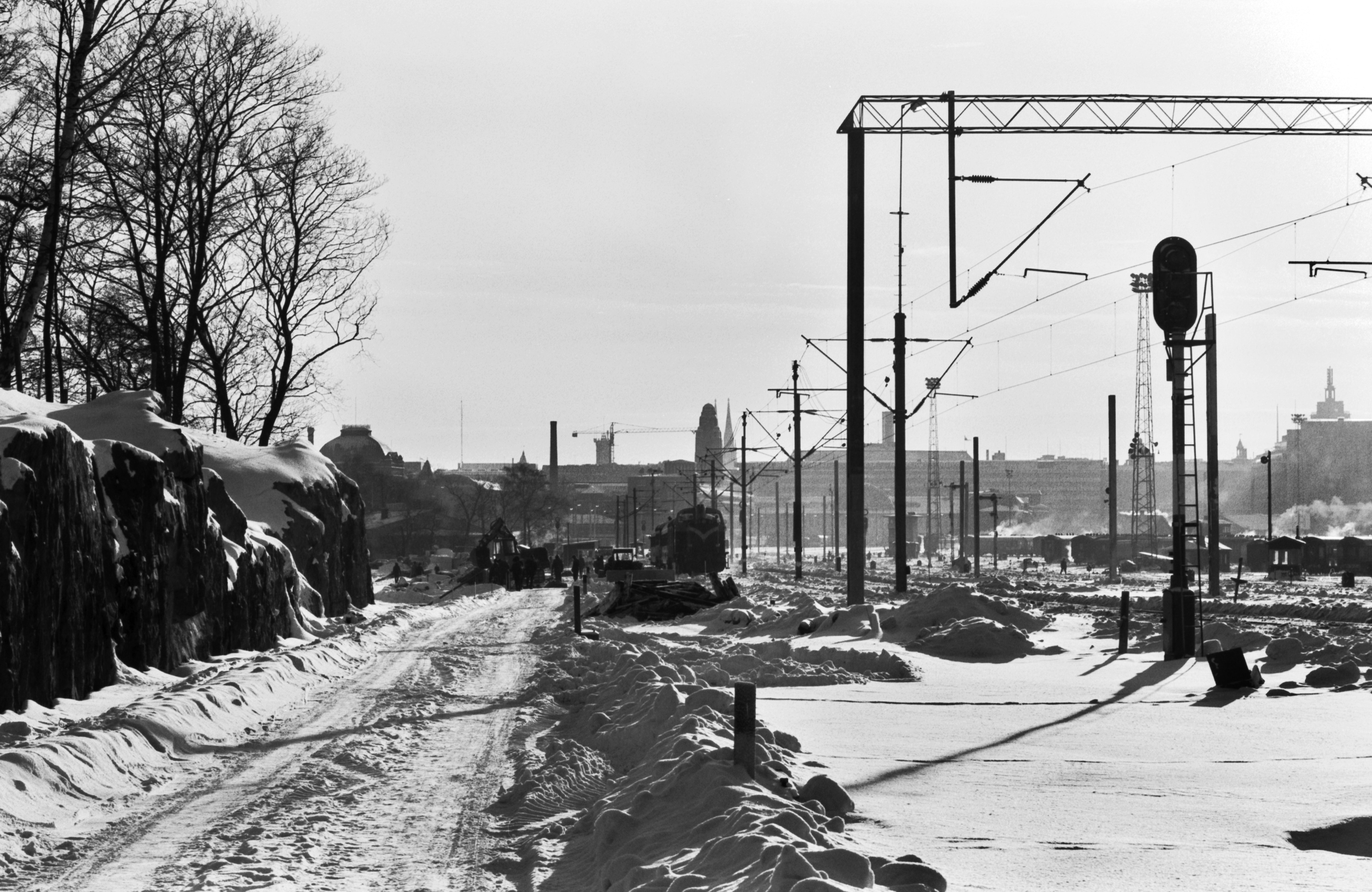 Miehiä töissä talvella lumisen pääradan varrella Eläintarhanlahden kohdalla. Kuva Linnunlaulun sillan suunnalta Helsingin rautatieasemalle päin.