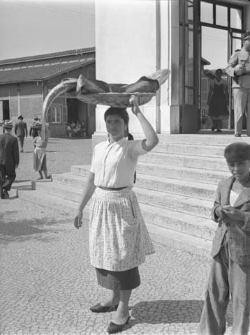 A woman carries big fish in a basket on her head in Lisbon.