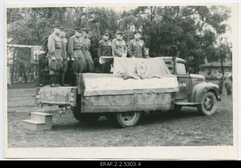 The officers of the 289th Attack Army Division stand in a decorated open truck in the event of a party event, names partially.