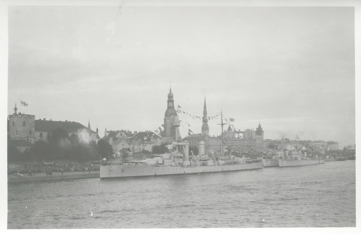 Pansarskeppet Drottning Victoria with jagarna EHRENSKÖLD och Nordenskjöld vid kaj i Riga. På kajkanten en thick folksamling. Form har uppenbarligen tagits i samband med Gustaf V statsbesök i Riga i juni 1929. It embroidery Fo229138 och Fo229417A.