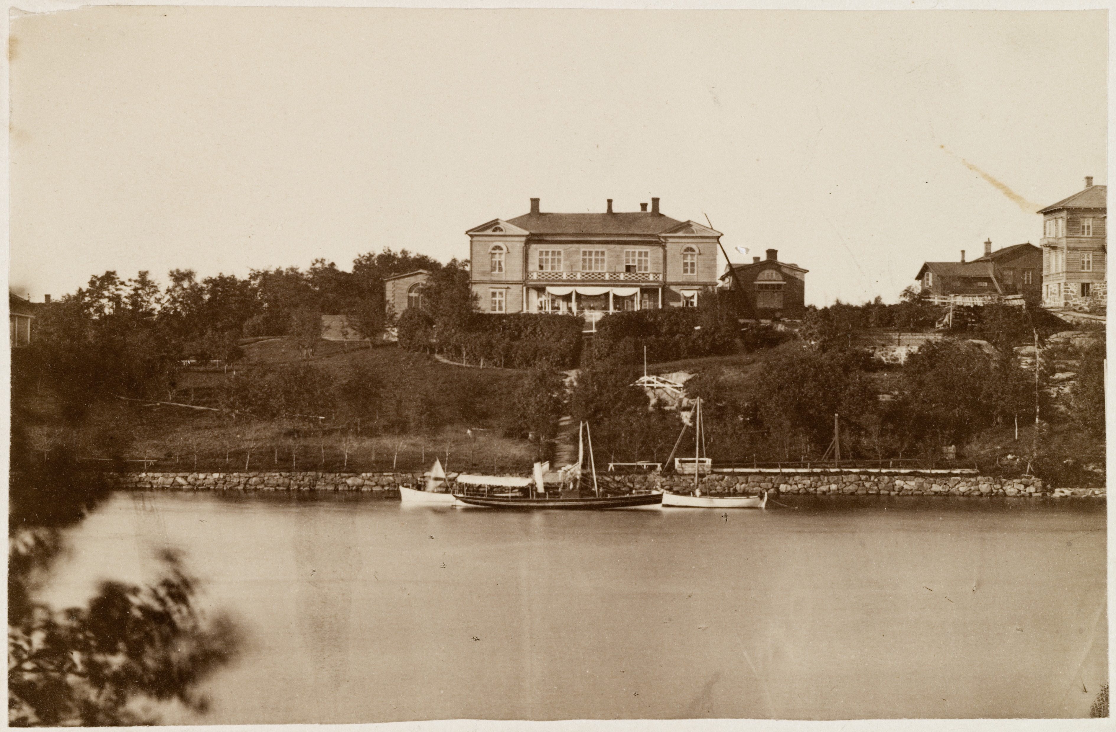 Huvila n:o 13 Itäisessä Kaivopuistossa, ennen paloa elokuussa 1879. Vanha osoite Huvilatie 13, nykyinen Kalliolinnantie.  Kuvan etualalla meri ja laituri, jossa  veneitä.