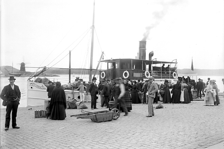 Marstrandsbolagets ångbåt "Tjörn" ankommande till Marstrand, med torghandlare från Tjörn och inlandet. Hedvigsholmen (Kvarnholmen) med väderkvarn syns i bakgrunden.