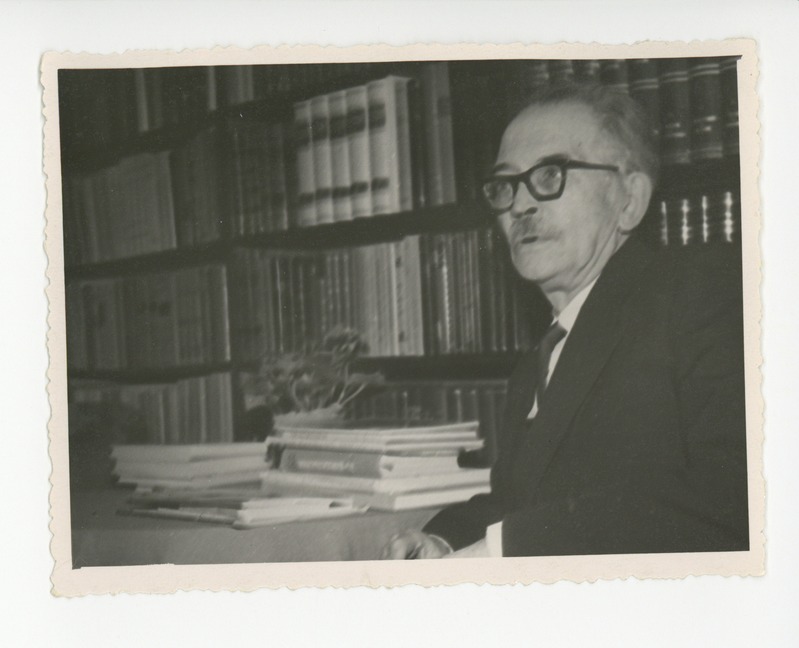 Friedebert Tuglas raamaturiiuli taustal istumas