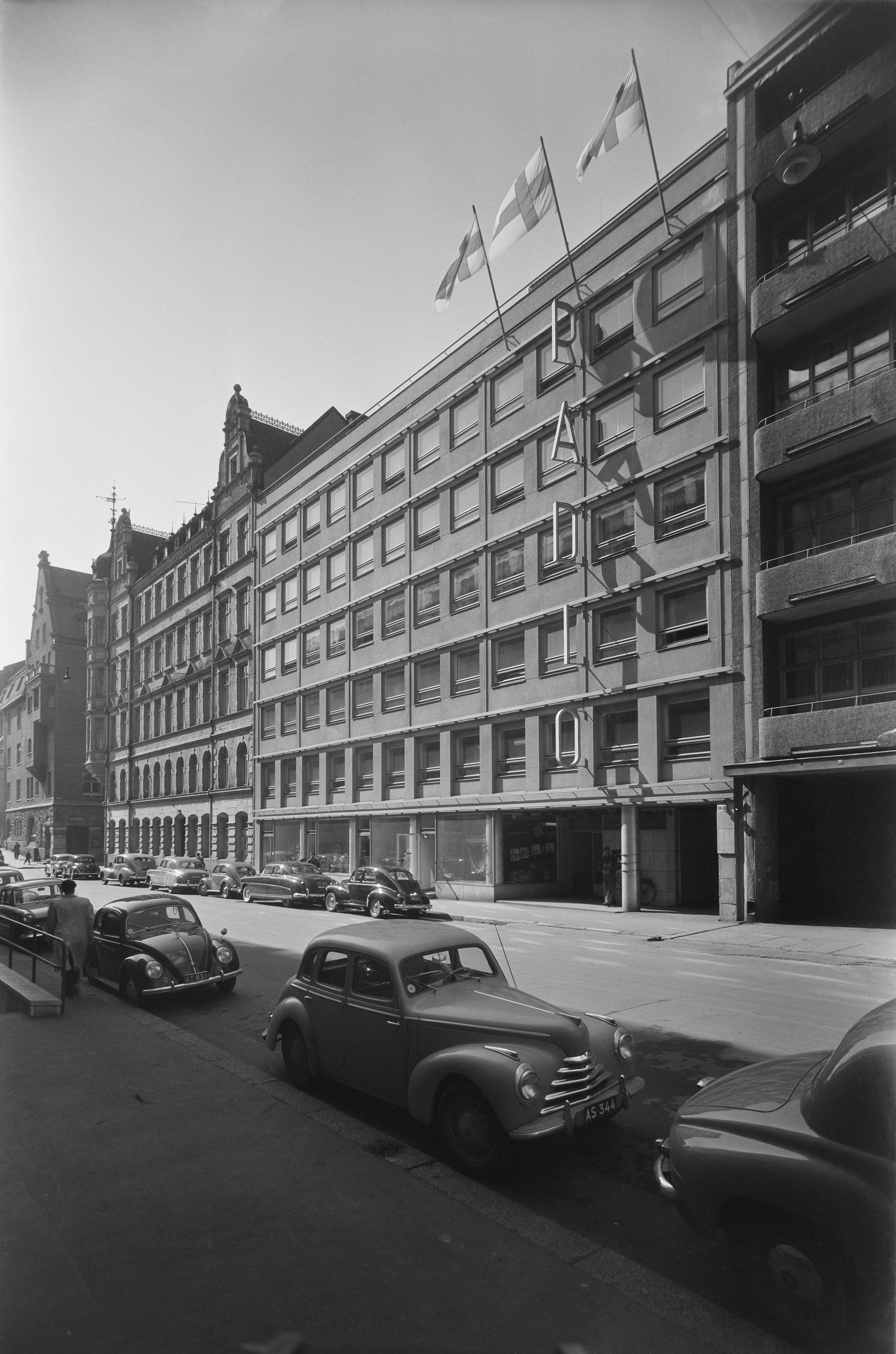 The Radio House, Unioninkatu, Helsinki, ca. 1953 - General Radio House, Unioninkatu 16 in Helsinki, on the wall of the building the text "radio", three Finnish flags in flagships, street view, cars parked on the street.