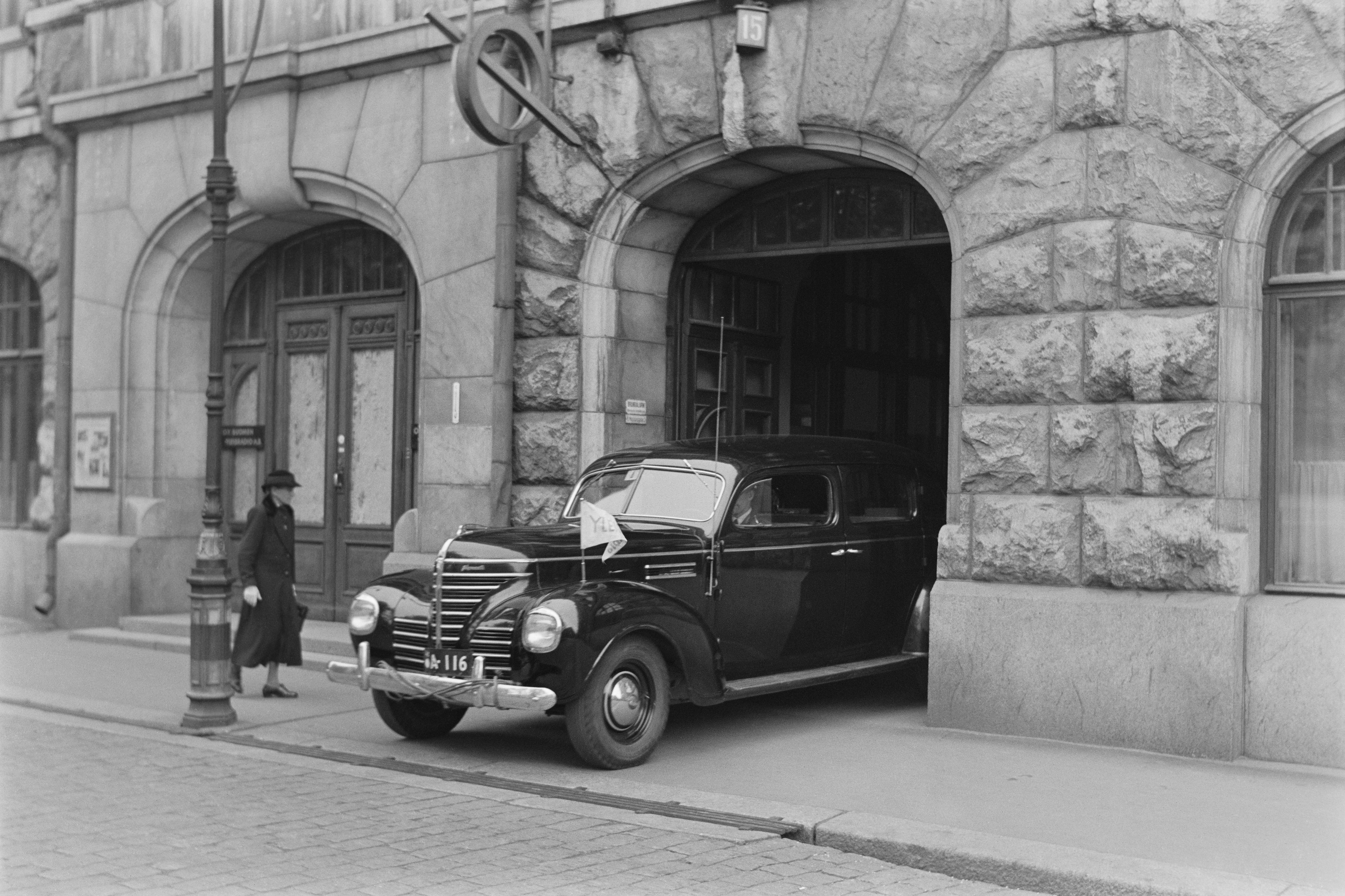 A car exits the Radio House gate is Fabianinkatu in Helsinki, 1930s - a passenger car with a general radio flag (car registration number A-116) driving out of the gate of the Fabianinkatu Radio House next to the main entrance (Fabianinkatu 15, Helsinki).