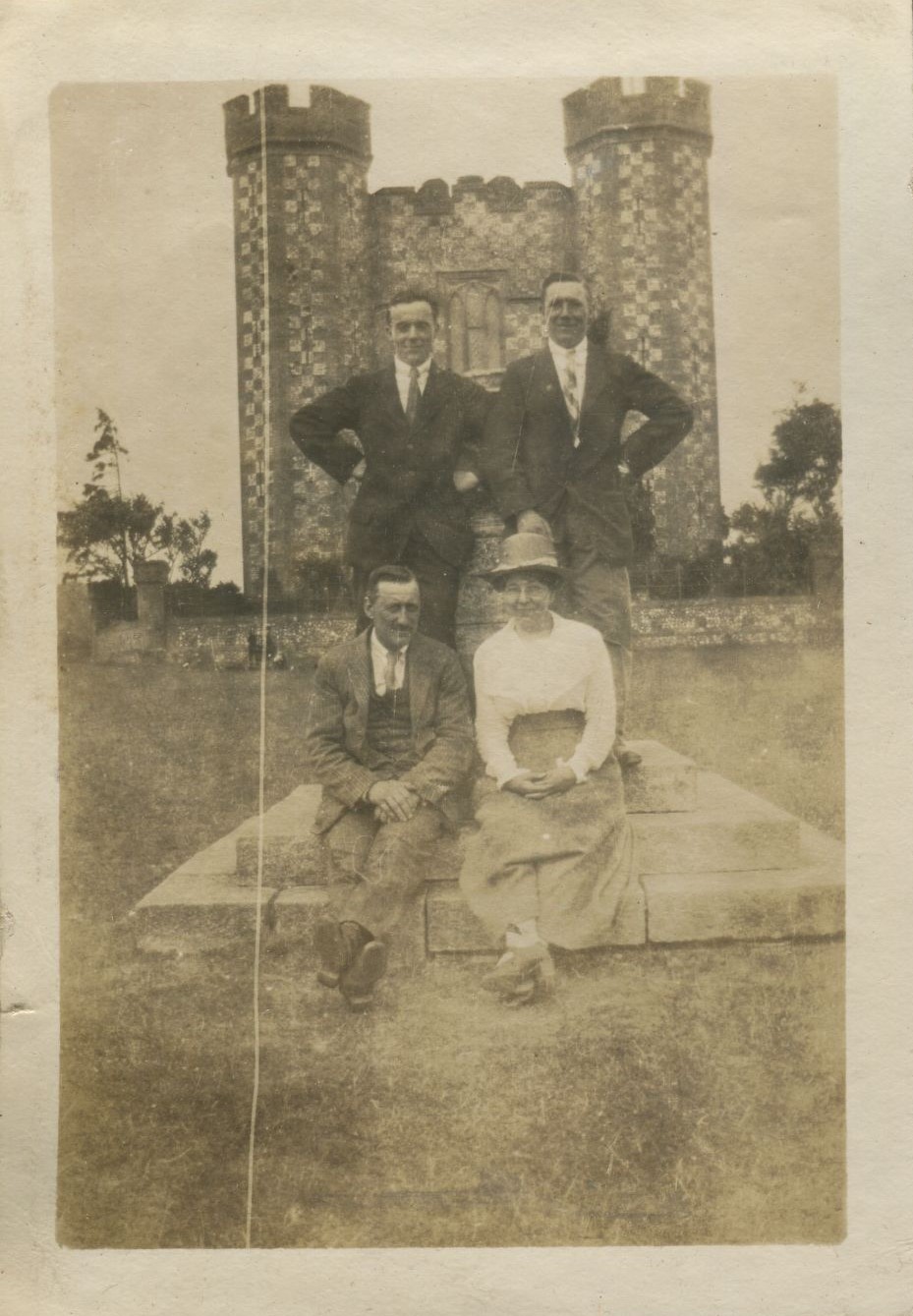 Posed photograph of two men standing in front of a castle with man and women seated in front of them