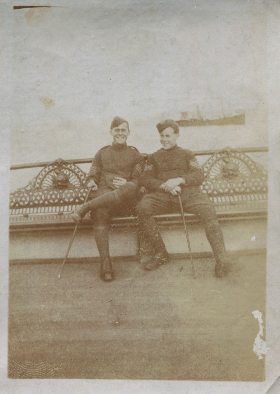 Two men in uniform seated on a bench with boat in the background