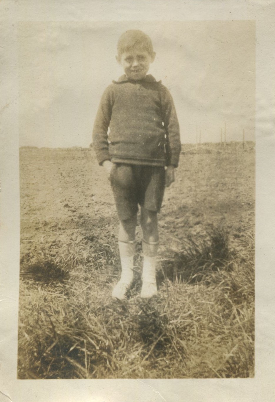Young boy standing on grass at the edge of a field