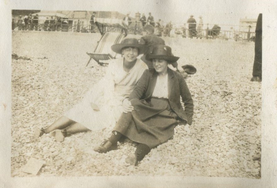 Two women seated on the beach in front of a deckchair
