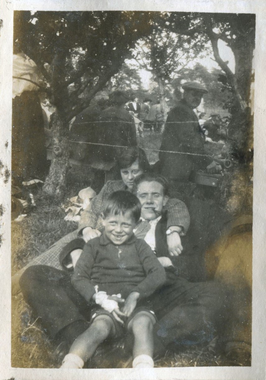 Young boy seated between the legs of a man, leaning back on a woman, Hassocks, 1920