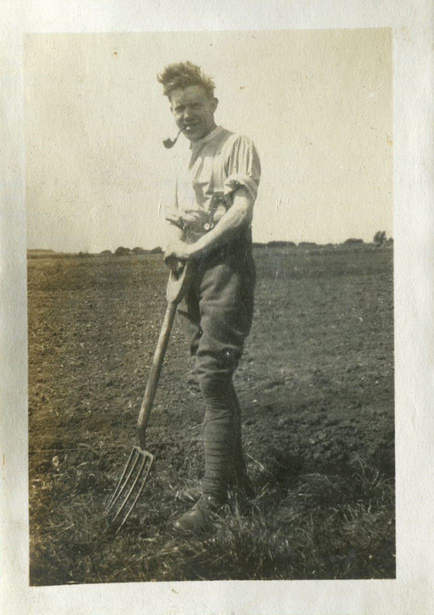 Man in field, smoking a pipe and holding a garden fork