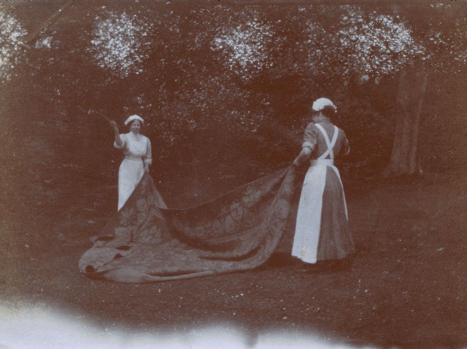 Two ladies beating a carpet in a garden