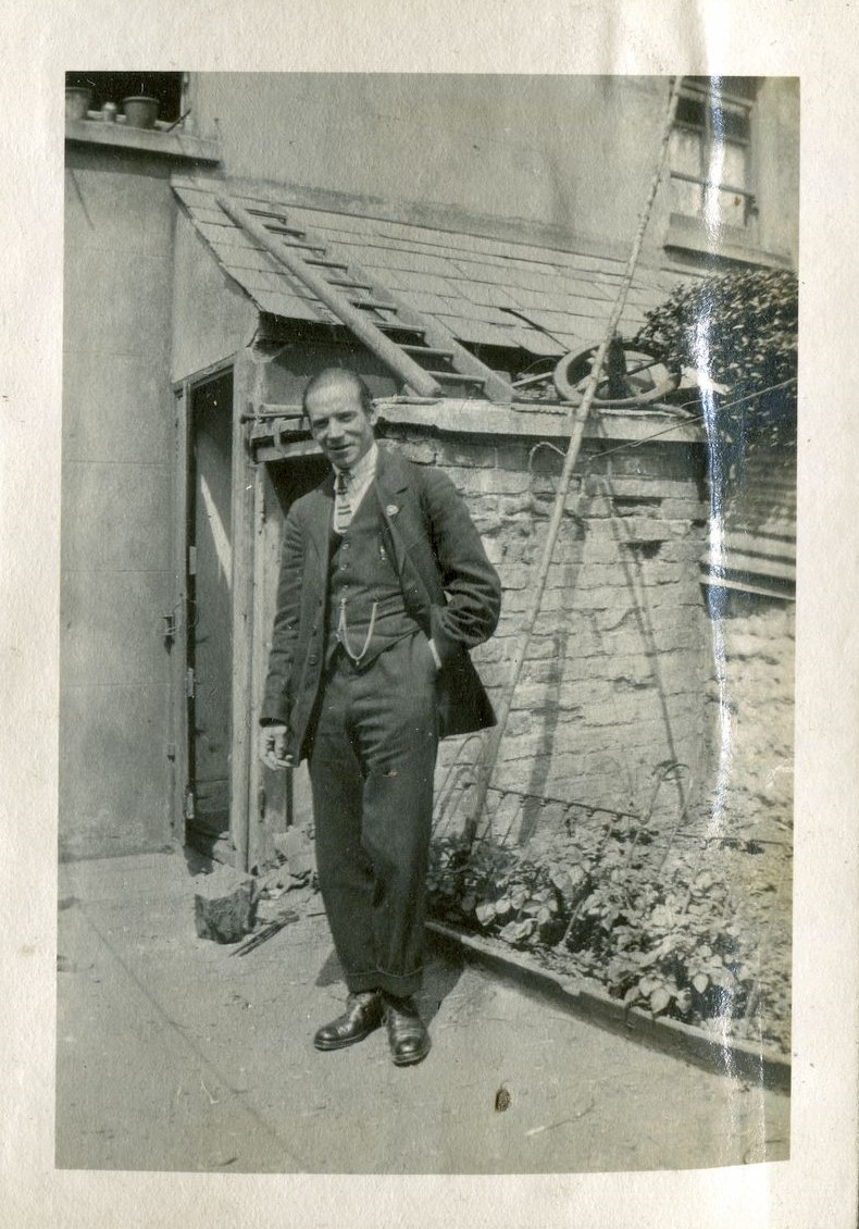 Man holding a biscuit,  standing in front of a house with a ladder on the roof, June 1922, Hove