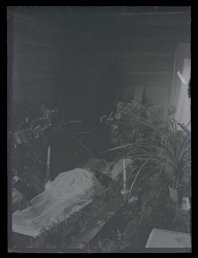 Matusefoto, naine avatud kirstus, kirstu ümber lilled ja küünlad.