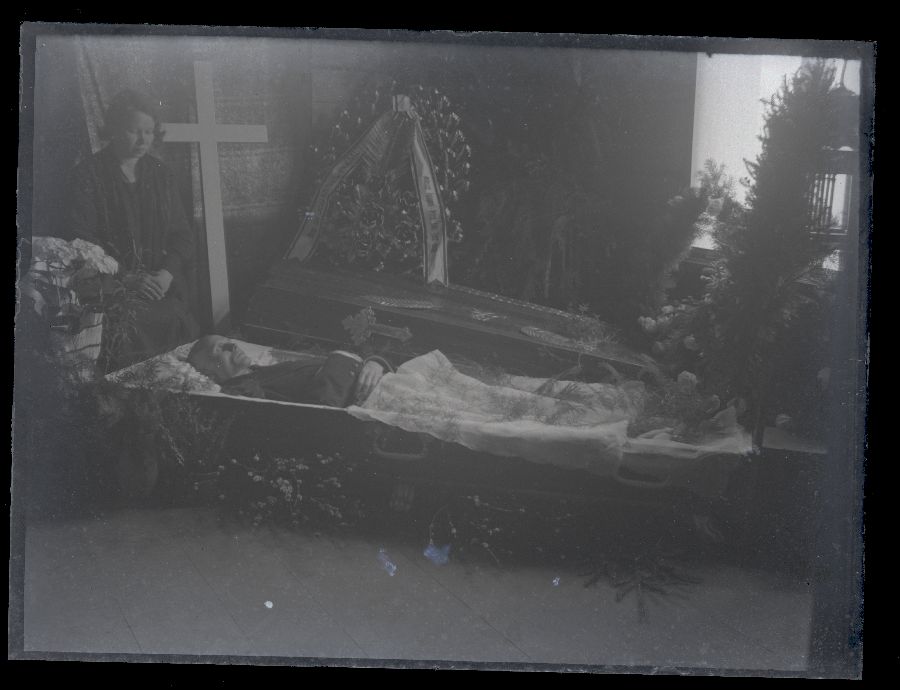 Matusefoto, mees lahtises kirstus, kirstu kõrval istub naine.