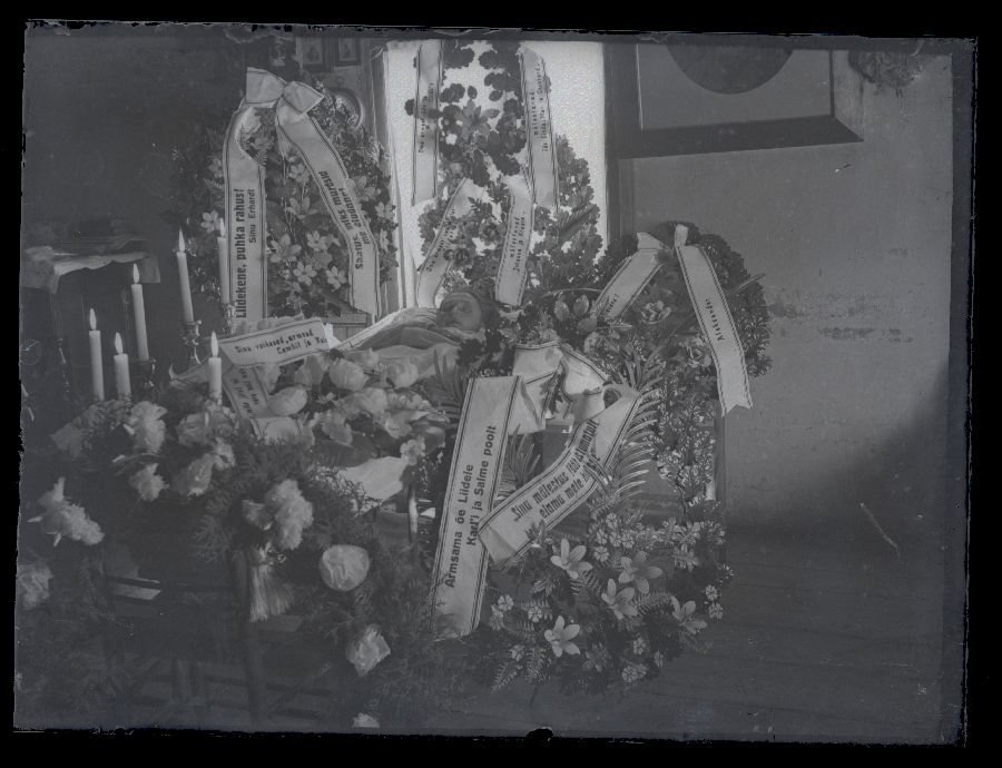 Matusefoto, naine avatud kirstus, kirst ümbritsetud lillepärgade ja küünaldega.
