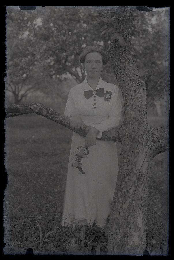 Naise täisportree, poseerib aias puu kõrval.