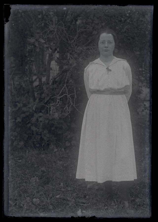 Valge kleidiga naine, pildistatud põõsa taustal.