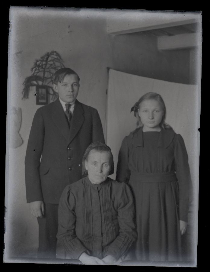 Vana naine ja kaks noorukit, pildistatud toas.
