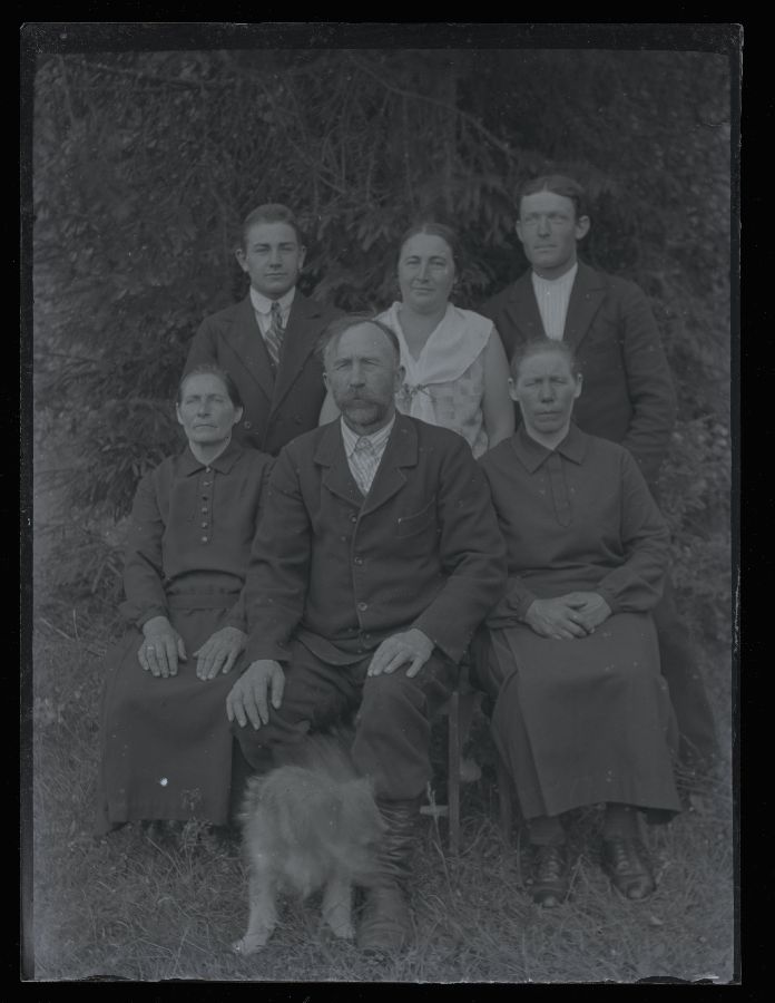Grupifoto, kuus inimest ja koer, pildistatud kuuskede taustal.