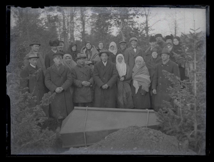Matusefoto, suletud kirst haua kõrval, kirstu taga seisavad matuselised.