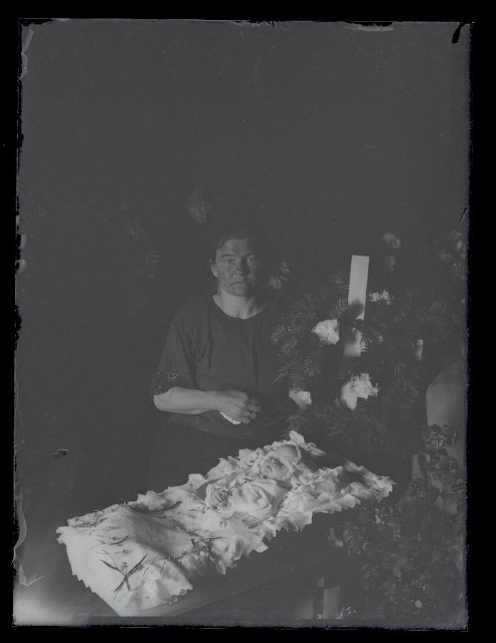 Matusefoto, väike laps avatud kirstus, kirstu taga istub naisterahvas.