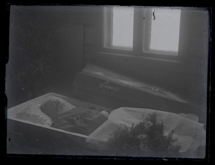 Matusefoto, vana mees avatud kirstus, kirstu taga akna all kirstukaas.