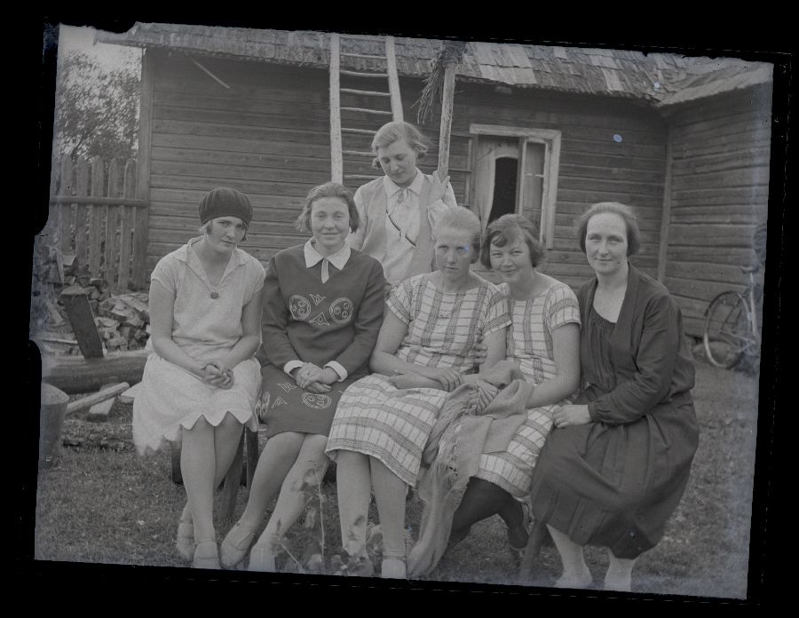 Grupifoto, kuus naist istuvad pingil, taustal maja.