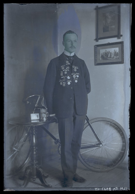 Johannes Parikase portreefoto, laual spordiauhinnad ja seljataga jalgratas, 20. sajandi I kümnendist.