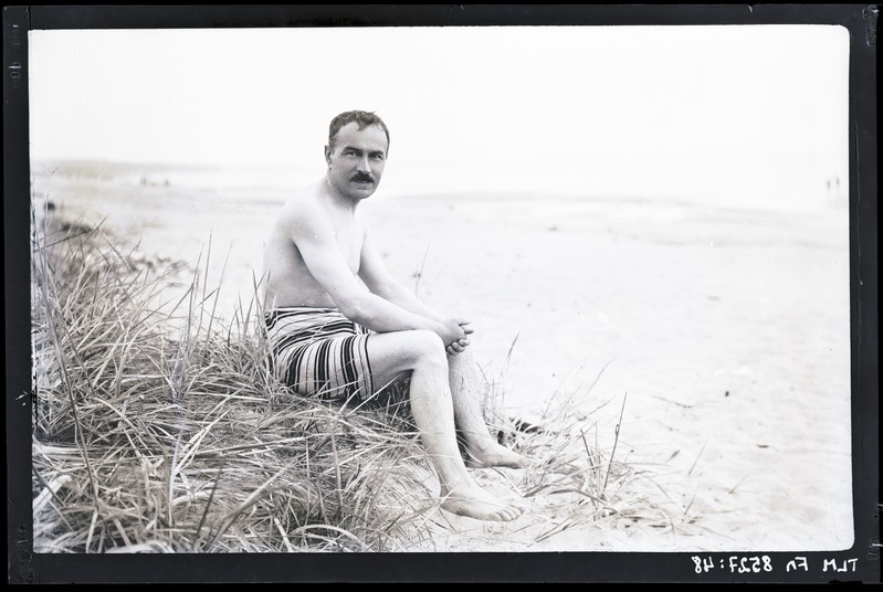 Meesfiguur, poolakt supelpükstes istumas mererannal, 20. sajandi II kümnend.