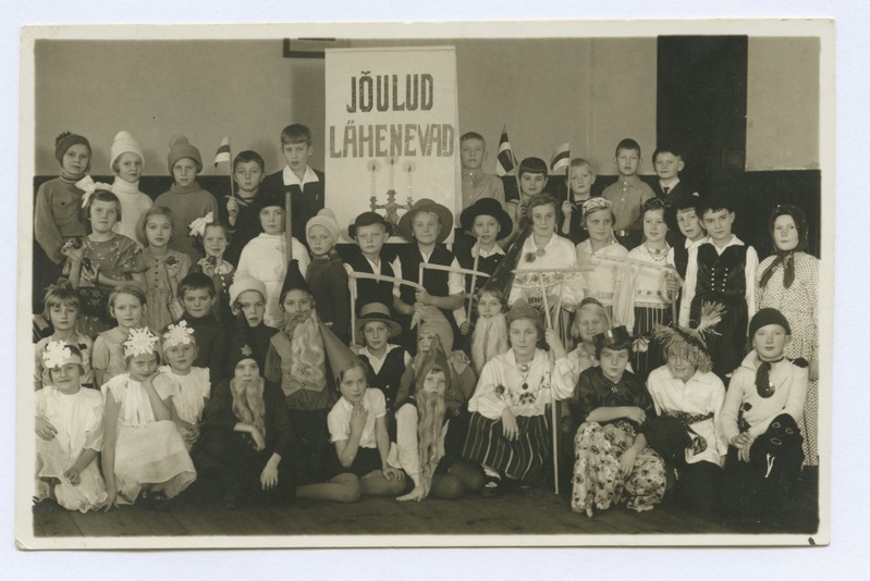 Grupipilt. Lapsed rahvariietes ja karnevalikostüümides eesti lipukestega. Plakat "Jõulud lähenevad". 1938.-1940. a